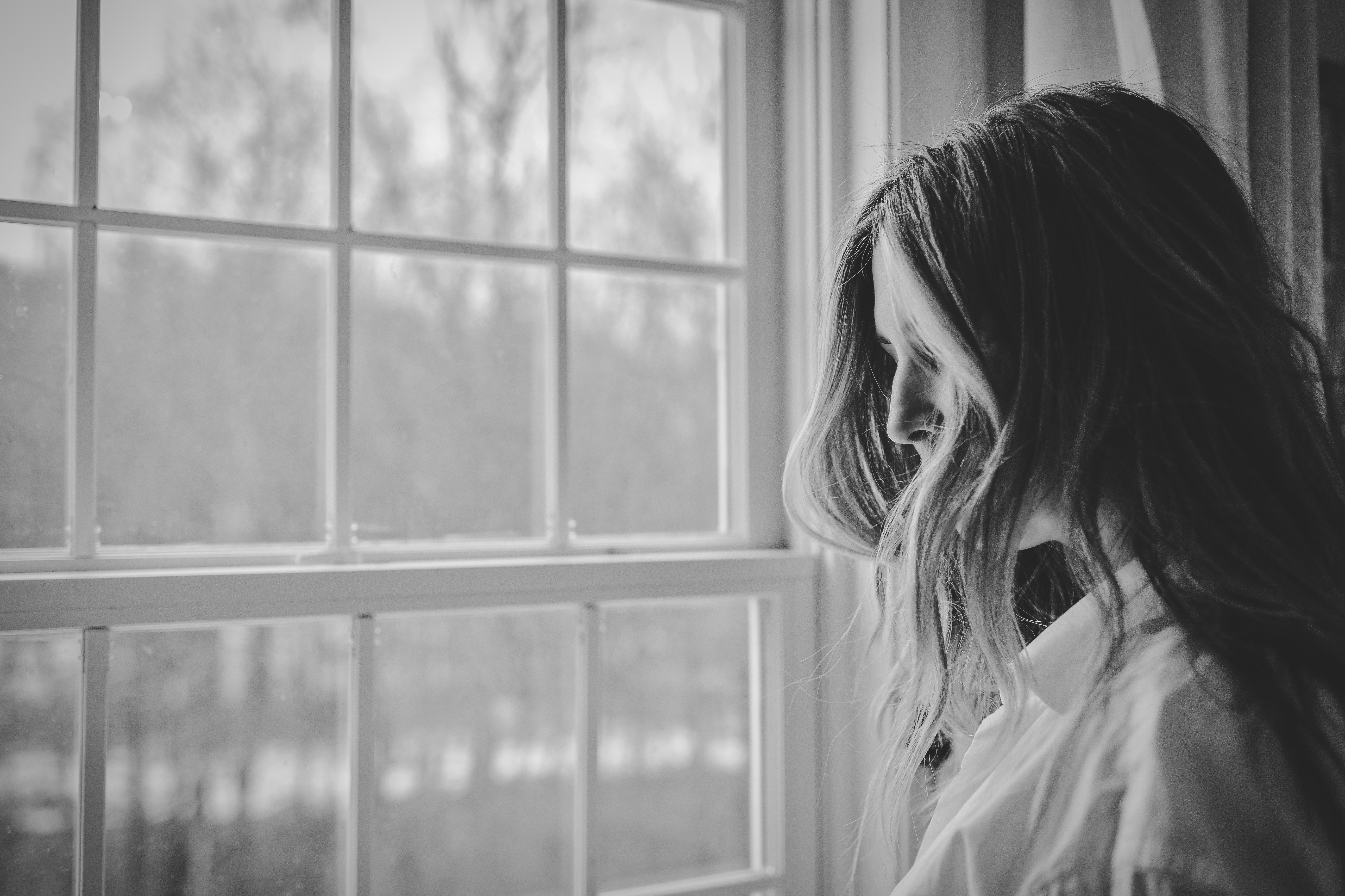 black and white. woman with face hidden by her hair looking out a window