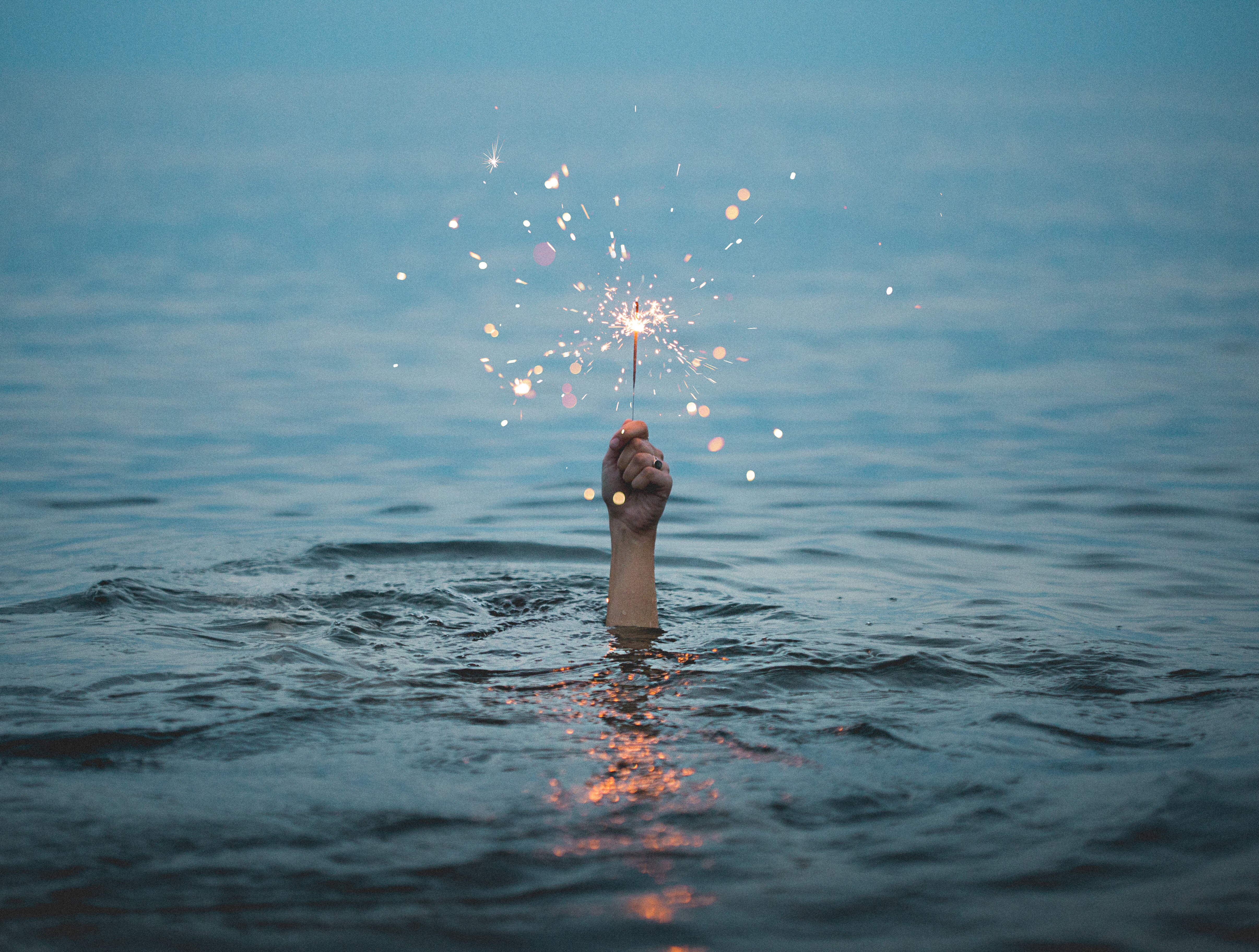 hand sticking out of water holding a sparkler