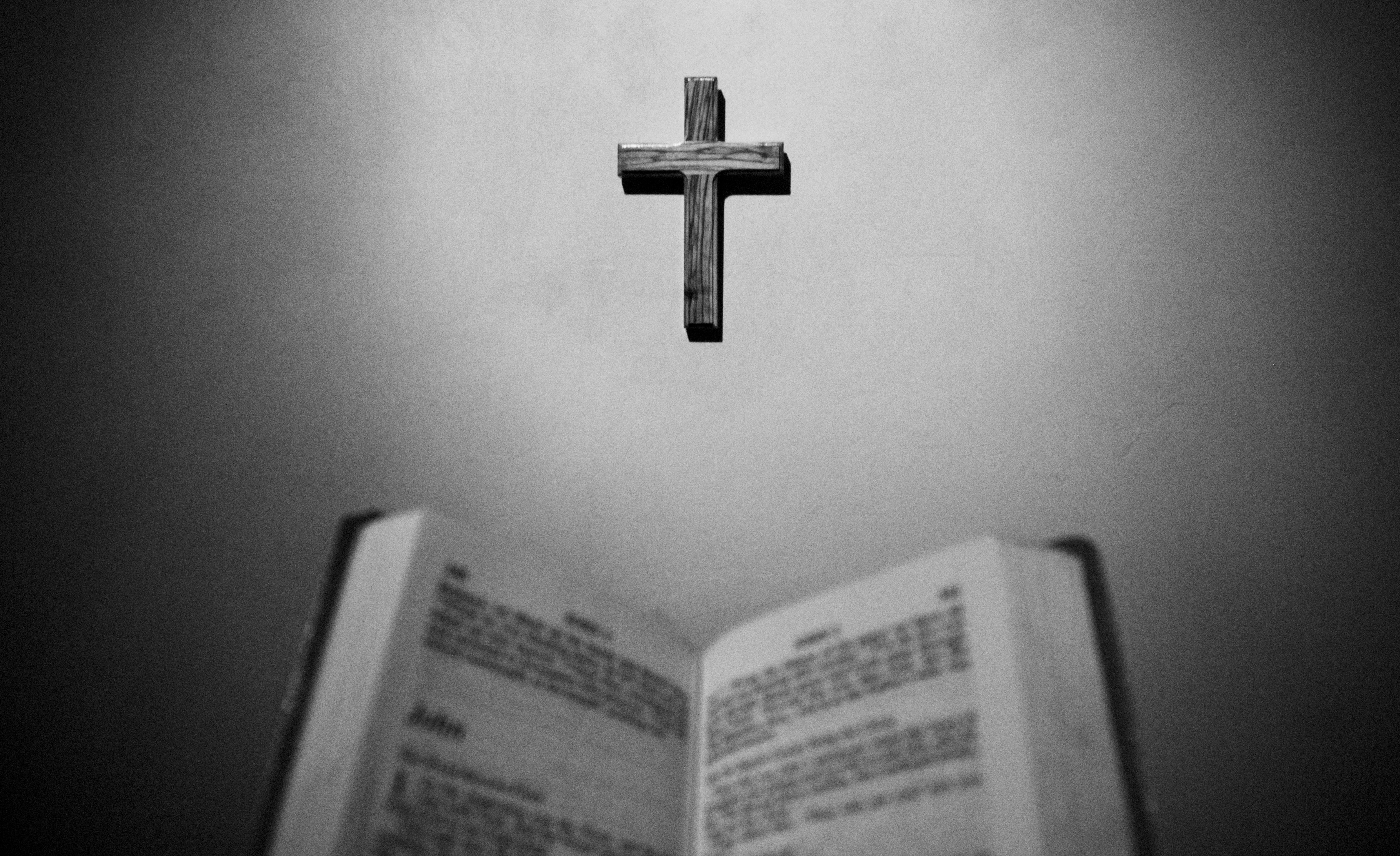 black and white. open bible with a small cross on the wall. 