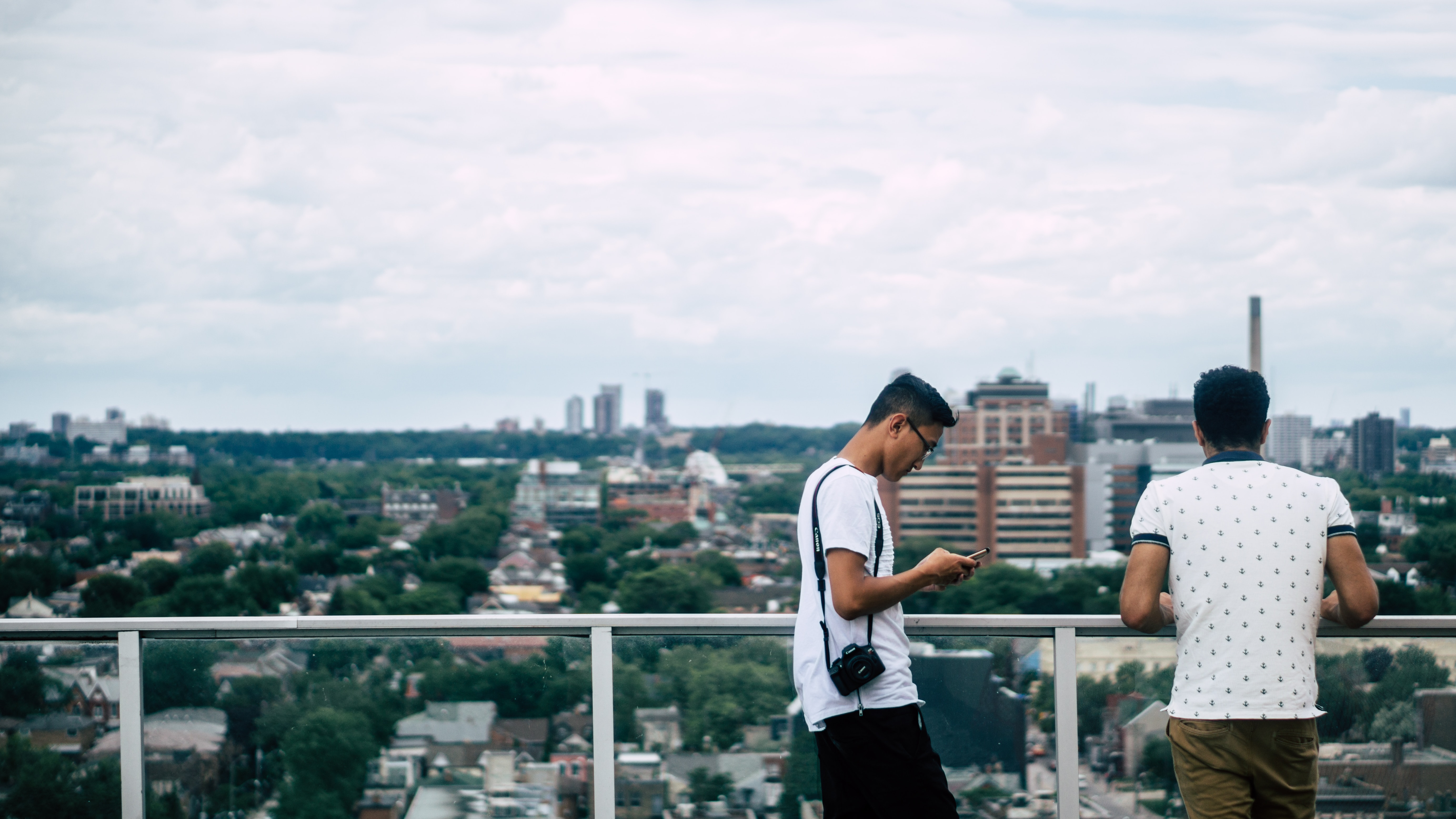 two men on a balcony overlooking the city, on man looking at his phone